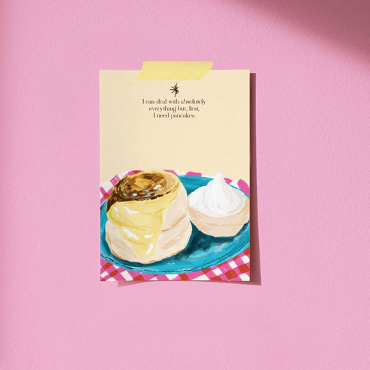 postal pegada sobre una pared rosa de unos panqueques y con el texto "I can deal with absolutely everything but, first, I need pancakes" de la artista Laura Ortiz