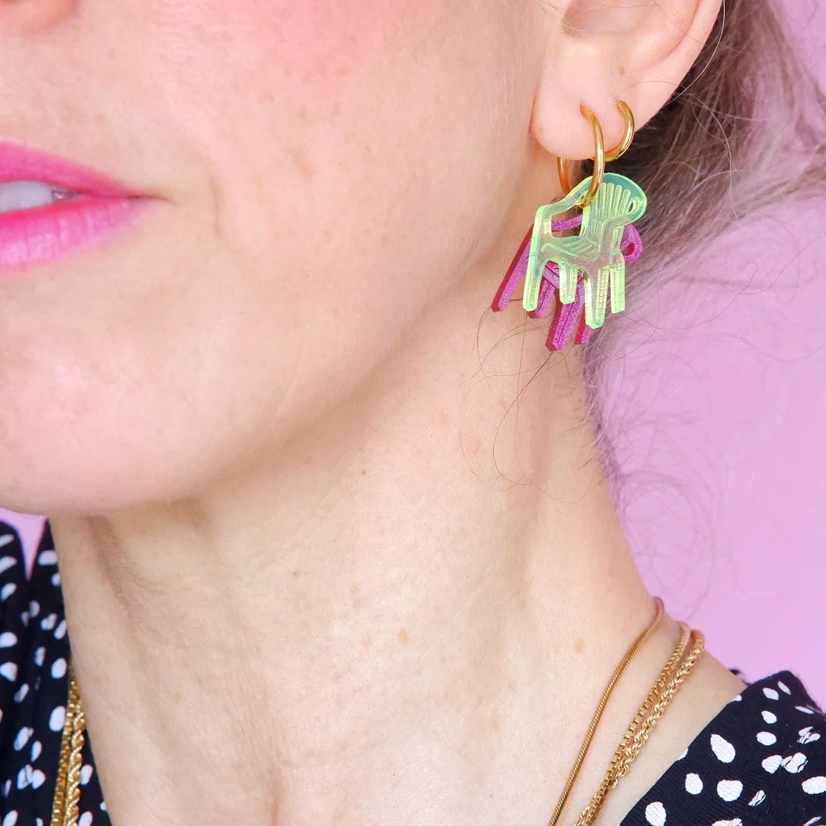 pendientes de metacrilato con arete dorado de la artista mitumi de unas sillas una encima de la otra, una en color lima translúcido y la otra en color magenta sólido