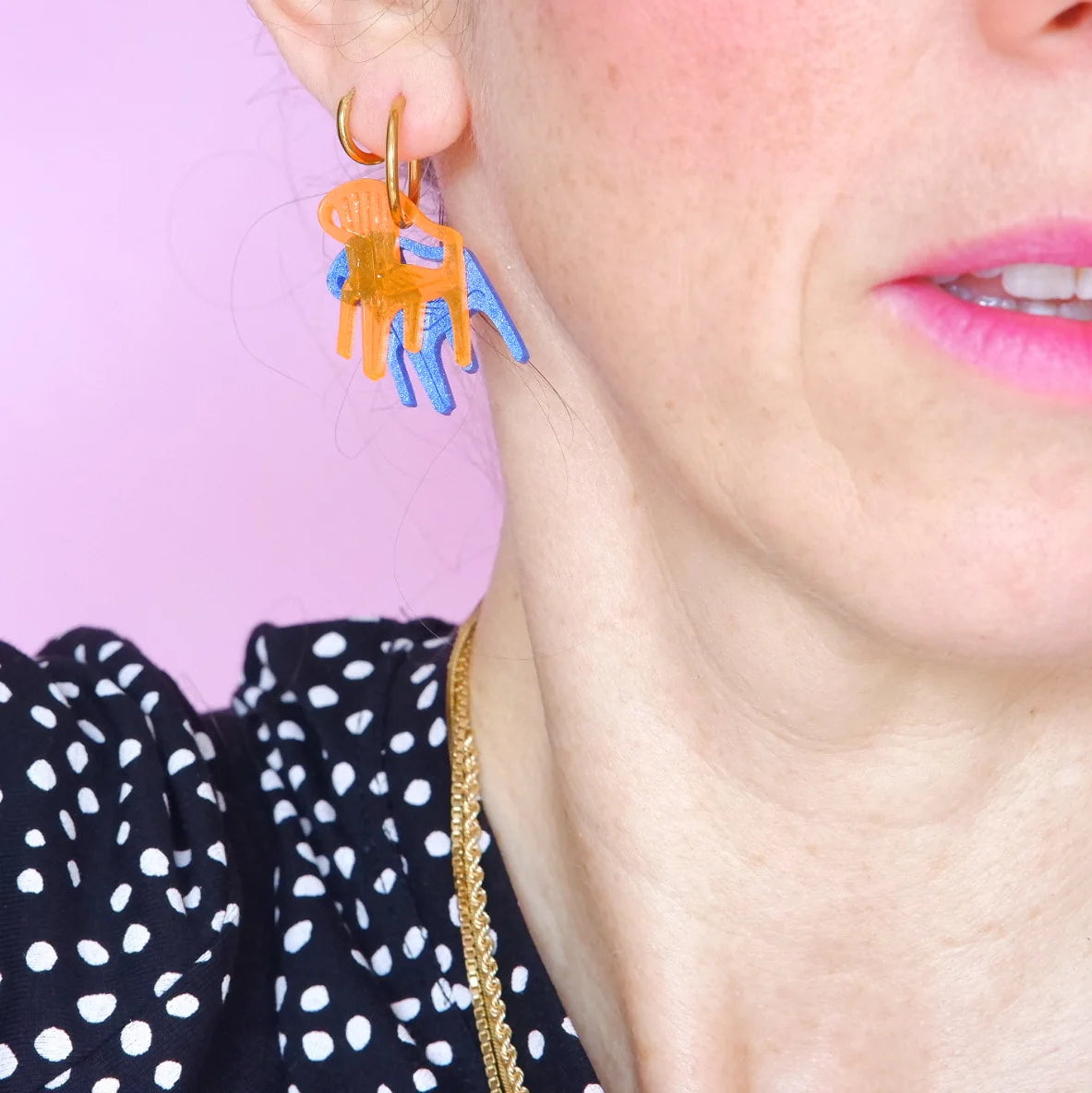 mujer llevando los pendientes de metacrilato con arete dorado de la artista mitumi de unas sillas una encima de la otra, una en color naranja translúcido y la otra en color azul sólido