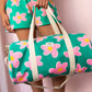 modelo cogiendo la bolsa de viaje Simon de la marca Hindbag en colaboración con We are Jolies en color verde con patrón de flores rosas con el centro amarillo y las asas beige