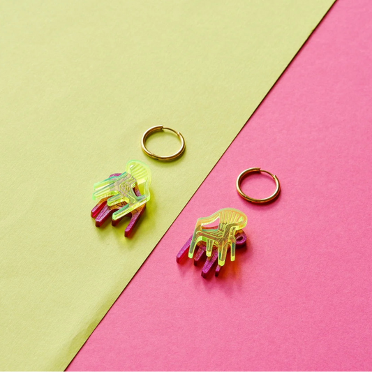 pendientes en forma de silla de color fucsia y amarillo neon encima de un fondo verde lima y magenta