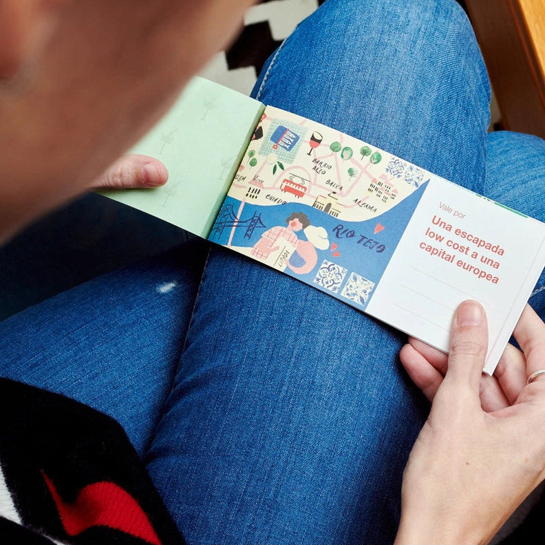 persona sujetando el talonario abierto sobre sus piernas con el taxto "una escapada low cost a una capital europea" y un dibujo de una persona con un mapa de fondo