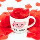 taza de porcelana con la imagen de una taza de té y la inscripción "té amo" cercada de pétalas rojas de rosa