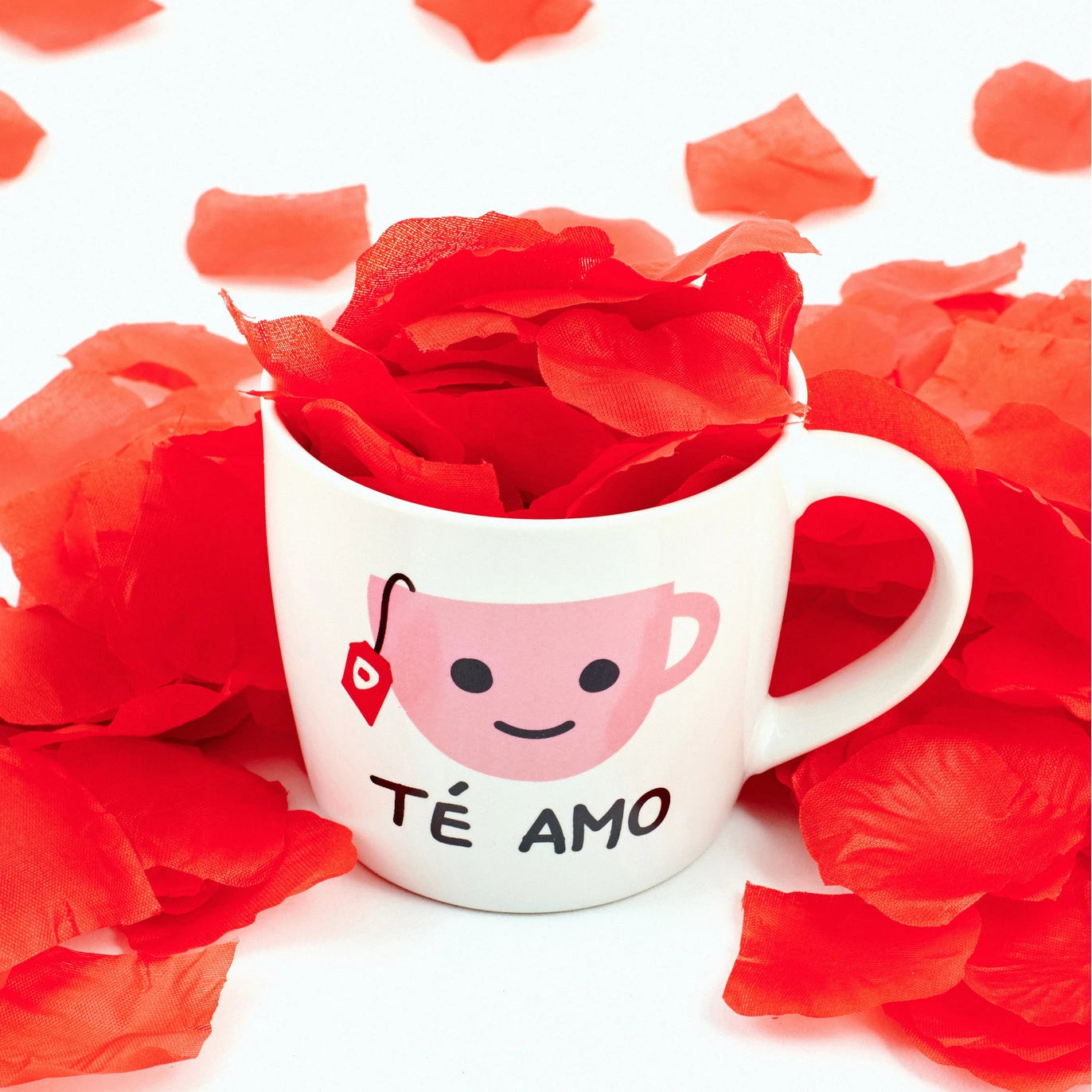 taza de porcelana con la imagen de una taza de té y la inscripción "té amo" cercada de pétalas rojas de rosa