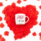 taza de porcelana con la imagen de una taza de té y la inscripción "té amo" en cima de un corazón hecho en pétalas rojas de rosa