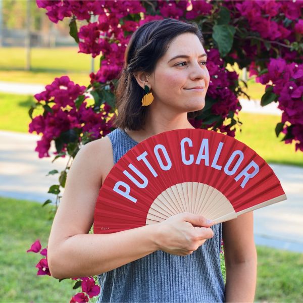 Chica abanicándose con un abanico rojo con letras blancas estampadas sobre fondo de buganvilla