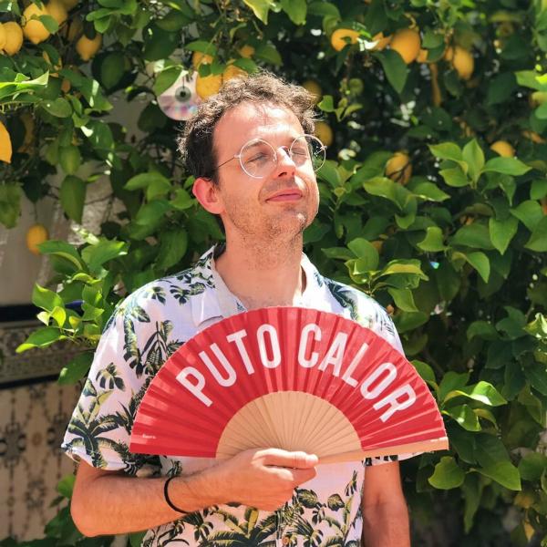 Hombre con camisa veraniega abanicándose con el abanico de puto calor en rojo junto a un limonero en Llerena, Badajoz