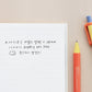 Bolígrafo de gel naranja amarillo y lavanda junto a una libreta con letras en coreano