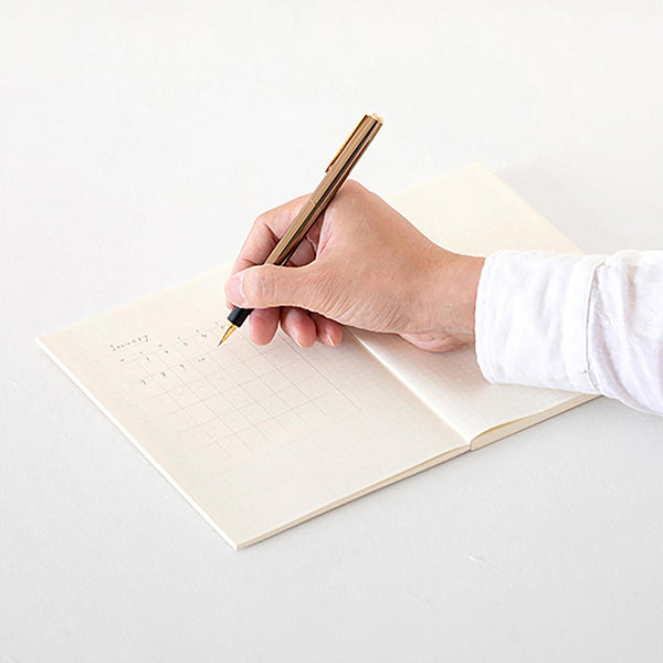 Persona con camisa blanca escribirndo en el calendario adhesivo de Midori con un bolígrafo dorado