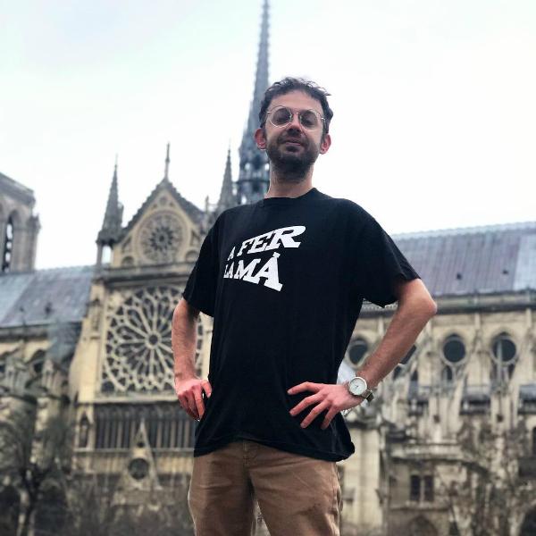 Chico de la tienda de regalos Gnomo de Valencia posa con la camiseta A fer la mà ante la iglesia de Notre Dame de París
