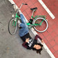 Mujer tumbada en el suelo del carril bici en Valencia con cara de fastidio después de haberse caído de la bicicleta verde con una camiseta de A fer la má
