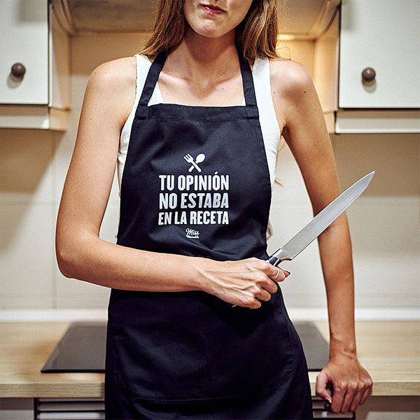 Mujer con un cuchillo de cocina y el delantal de tela negro con bolsillo y el mensaje "Tu opinión no estaba en la receta" 