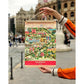 Chico sosteniendo una lámina con ilustración del centro histórico de Valencia de la firma de souvenirs originales Atypical enmarcada en colgadores de madera en la Estación del Norte