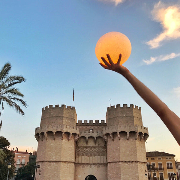 Lámpara con forma de luna mediana sujetada por una mano delante de las Torres de Serranos en Valencia
