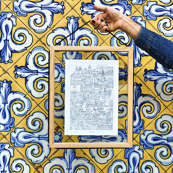 Mano sujetando un marco de madera y cristal con una ilustración de Rashomon sobre una pared de azulejos en Valencia