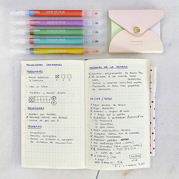 Cuaderno de cuadros tamaño A5 para escribir o dibujar rodeado de rotuladores de colores y post-it de colores