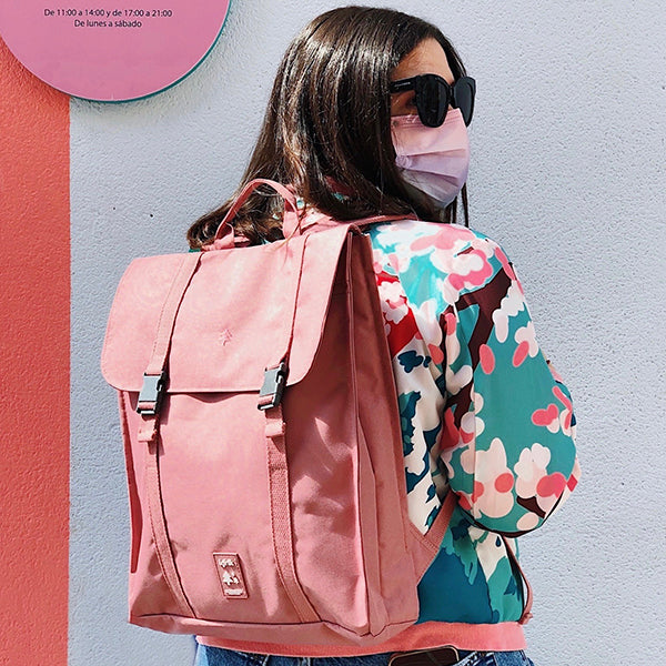 Persona llevando una mochila grande, de color rosa palo y dos cierres con correa.