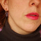 Perfil de mujer con los pendientes de aro dorados con un colgante de metacrilato morado translúcido con forma del símbolo de la mujer
