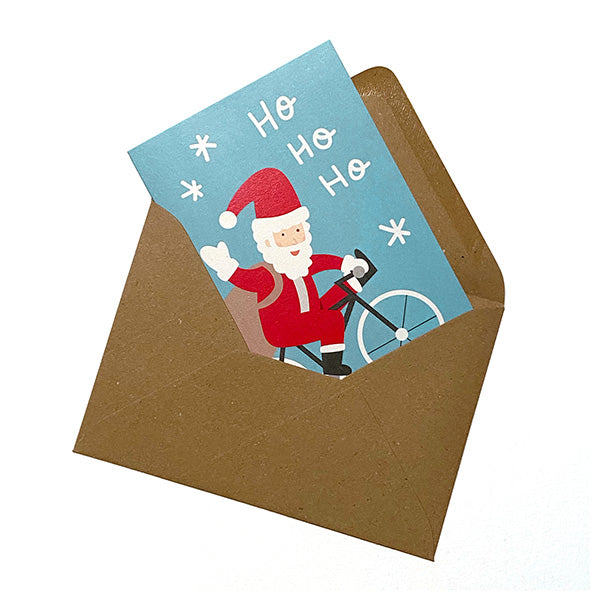Postal de Navidad dentro de un sobre marrón craft con dibujo de papá noel en bicicleta