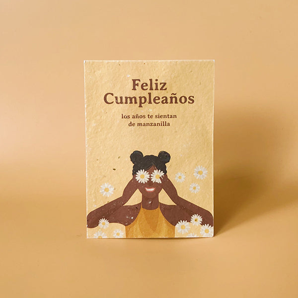 Tarjeta postal ecológica con semillas Feliz Cumpleaños de Sheedo xon una chica negra con dos moños y margaritas en los ojos