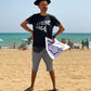 Chico con camiseta negra con inscripción A fer la mà, gorro y sable de pirata y un mapa del tesoro en la playa