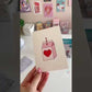 Persona enseñando el dispensador de celo en forma de noria y una tarjeta postal.