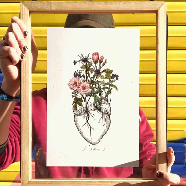 Ilustración de Laura Agustí de un corazón anatómico del que brotan rosas salvajes, cardos y nomeolvides en tamaño A4 en un marco de cristal
