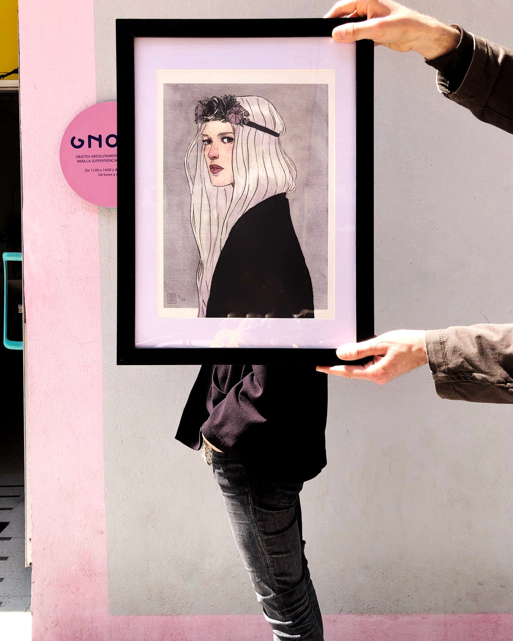 Una persona posa con un marco negro para fotos o prints con una lámina de Esther Gili