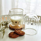 Dos vasos de cristal con forma de gato, uno con leche y el otro vacío y del revés, sobre una bandeja con galletas.