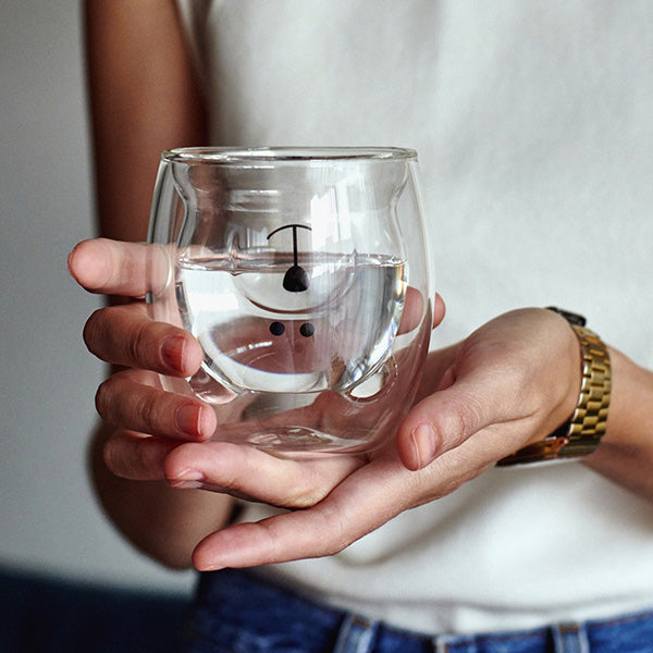 Una persona sujeta el vaso de cristal con forma y cara de oso lleno de agua.
