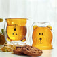 Dos vaso de vídrio de doble pared con la silueta de un oso color ámbar en el interior, uno al derecho y otro al revés en una mesa con galletas